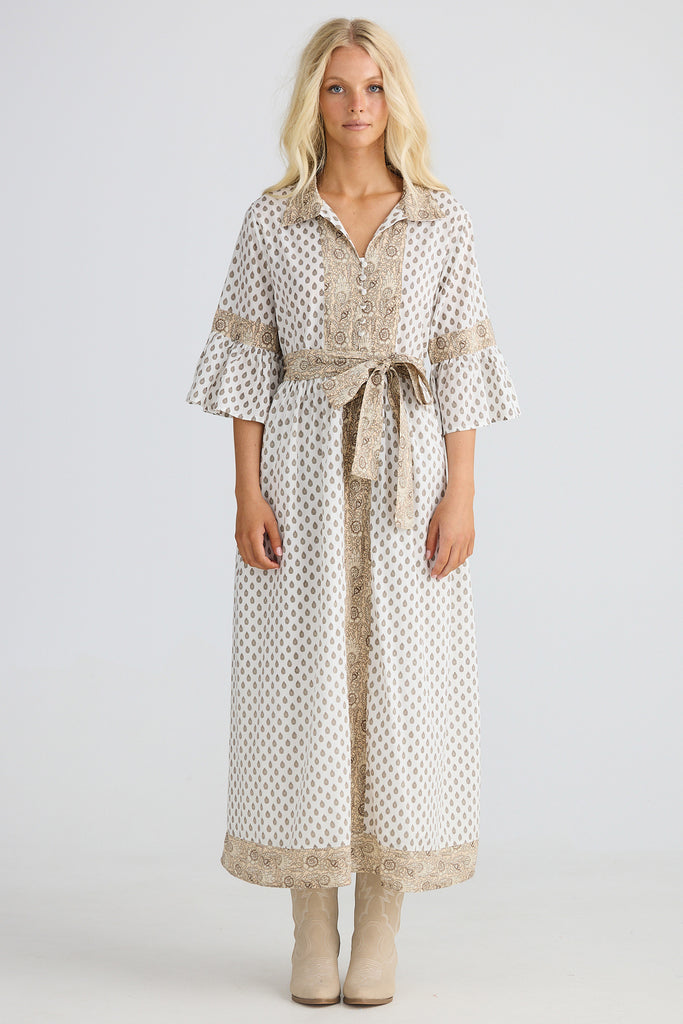 Woman wearing a long, patterned dress with a belt on a white background