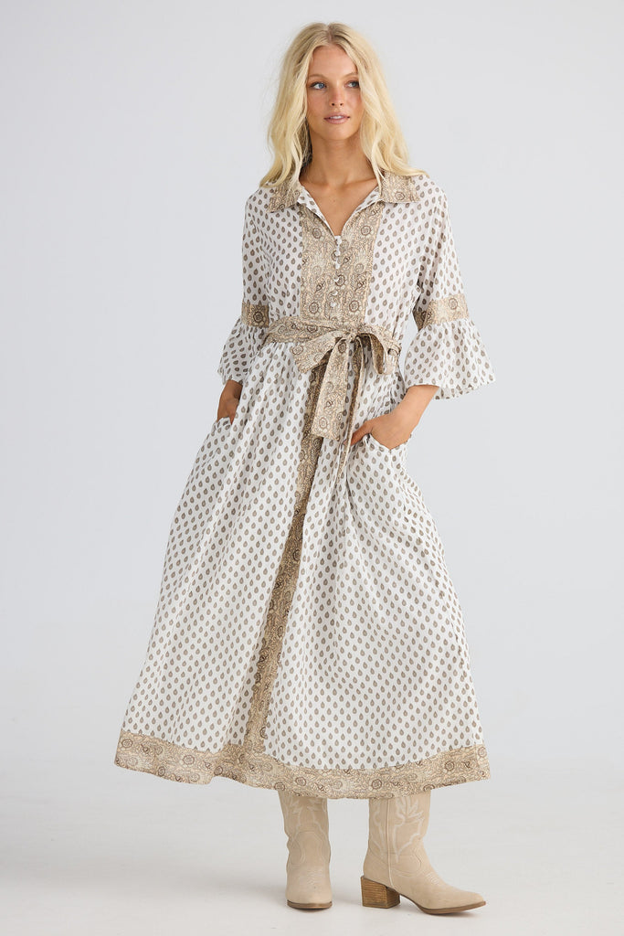 Woman wearing a long, patterned dress with a belt on a white background