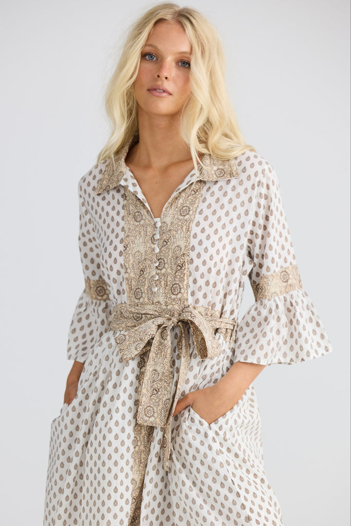 Woman wearing a patterned dress with a belt against a plain background