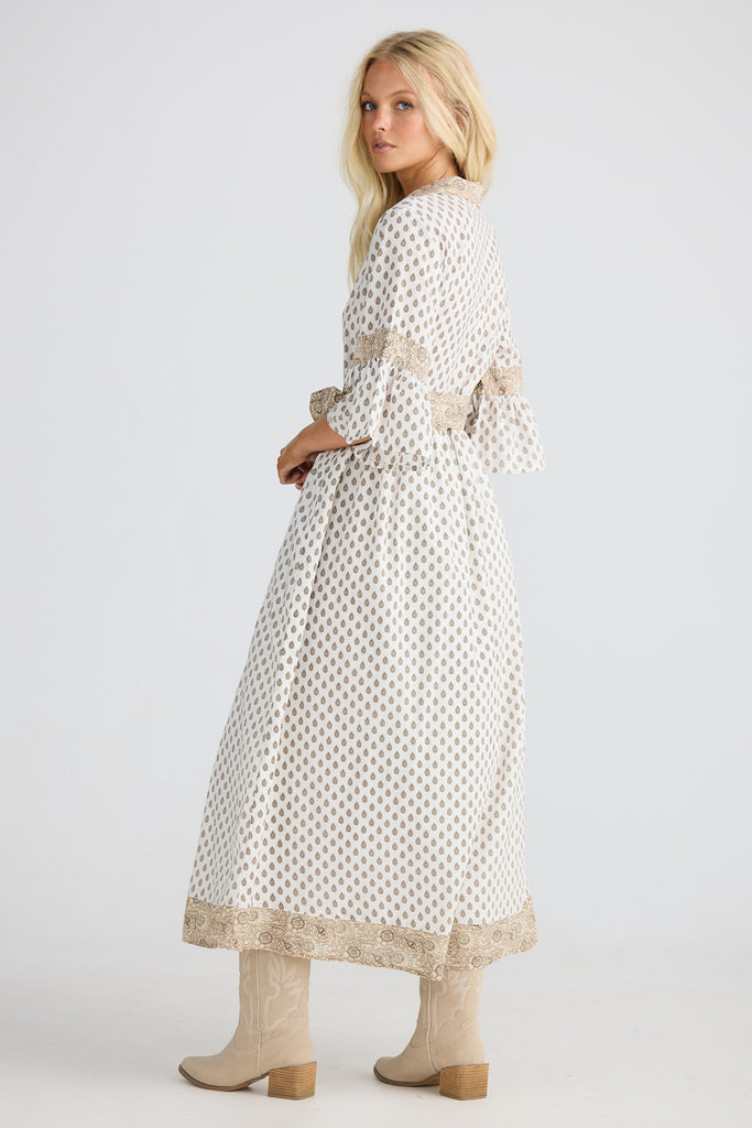 Woman wearing a long, patterned dress with lace details on a white background