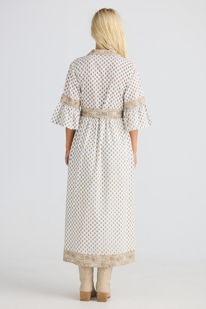 Woman wearing a long, patterned dress with lace trim on a white background