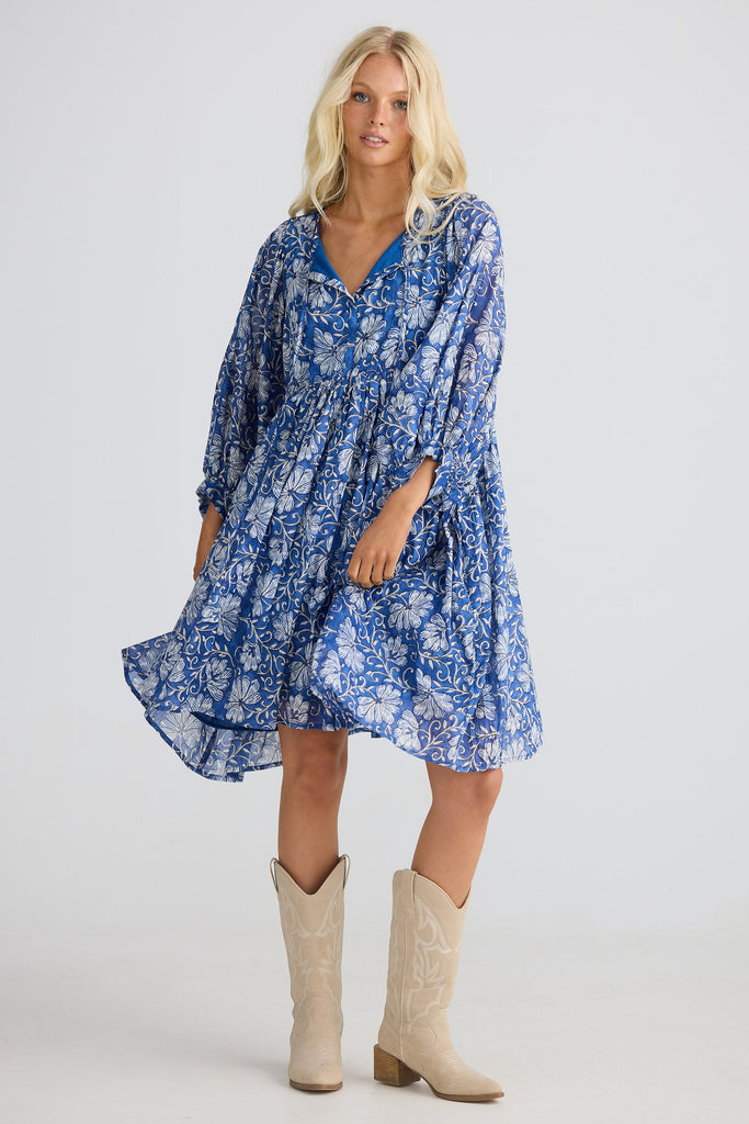 Woman wearing a blue floral dress and beige cowboy boots on a white background