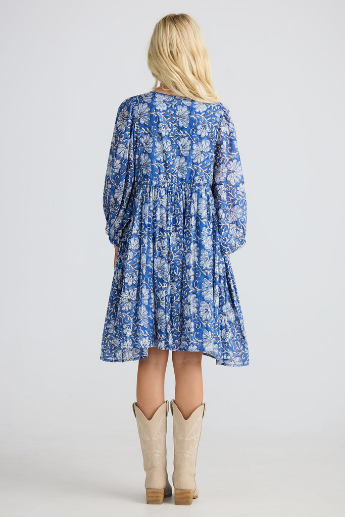 Woman wearing a blue floral dress with beige cowboy boots on a white background