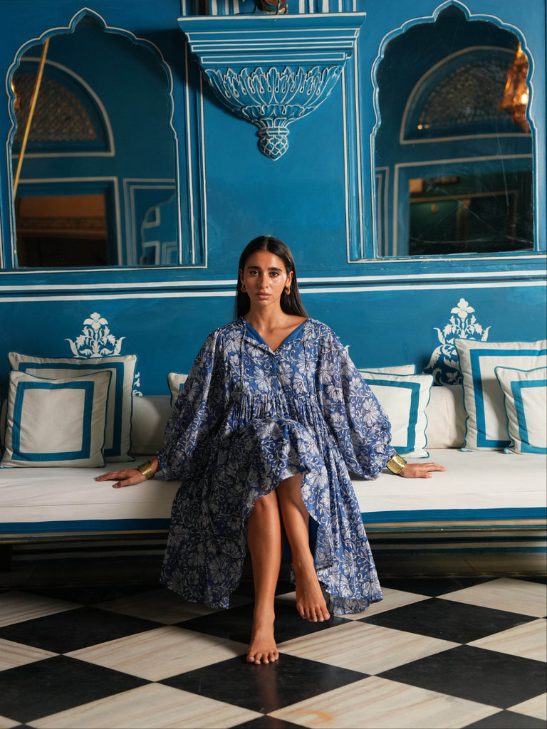 Woman in a blue dress sitting on a couch in a room with blue walls and decorative elements.