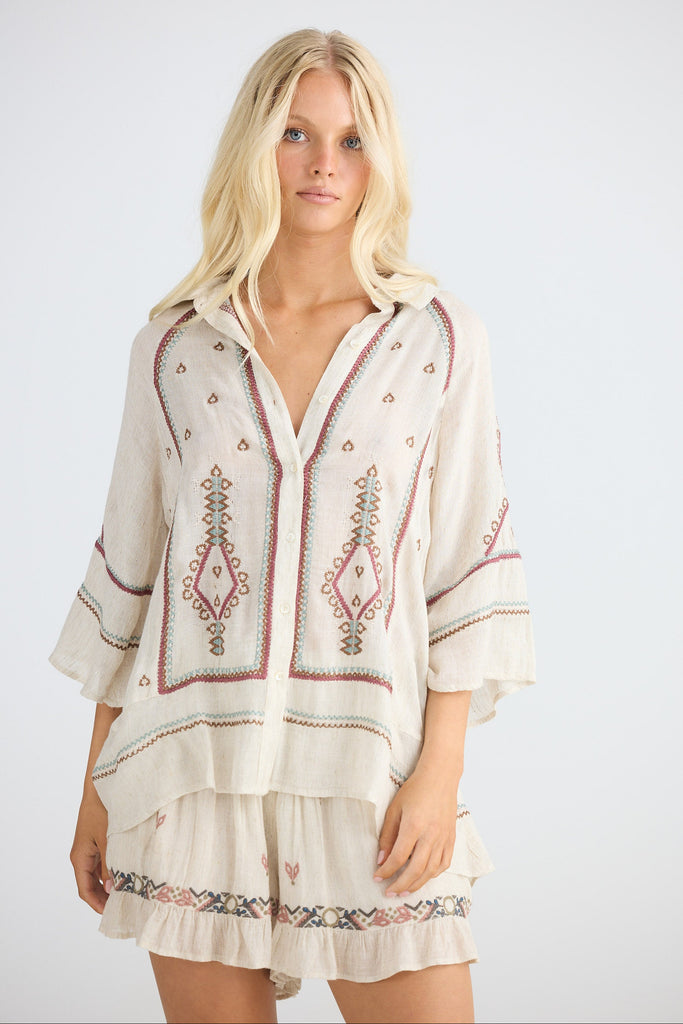 Woman wearing a beige embroidered shirt and shorts on a white background