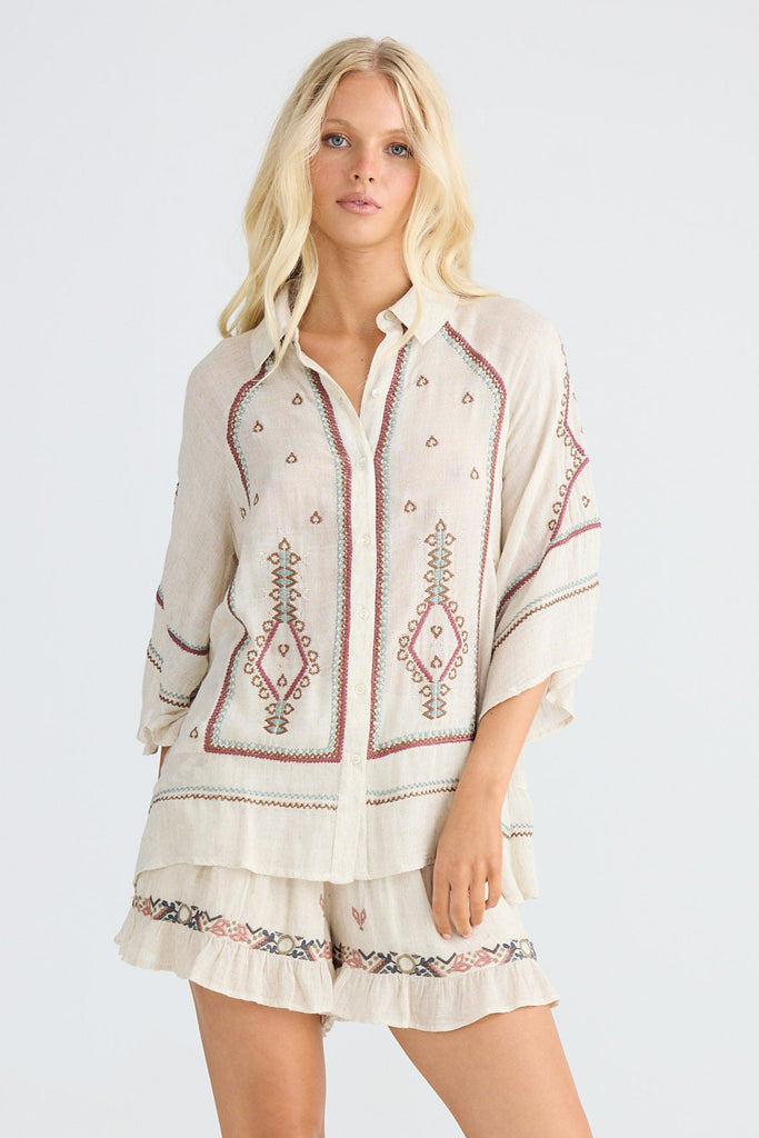 Woman wearing a beige embroidered shirt and shorts on a white background