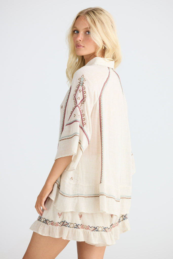 Woman wearing a beige embroidered shirt and shorts on a white background