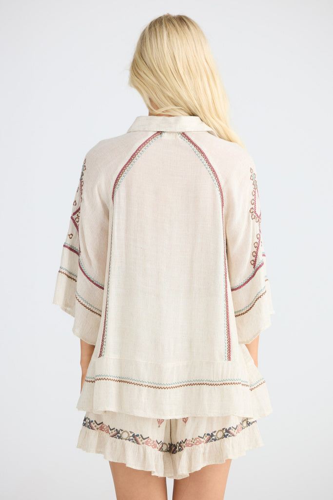 Woman wearing a beige embroidered shirt and shorts on a white background