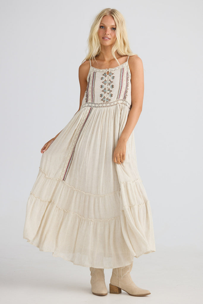 Woman wearing a long, light-colored dress with embroidery on a white background