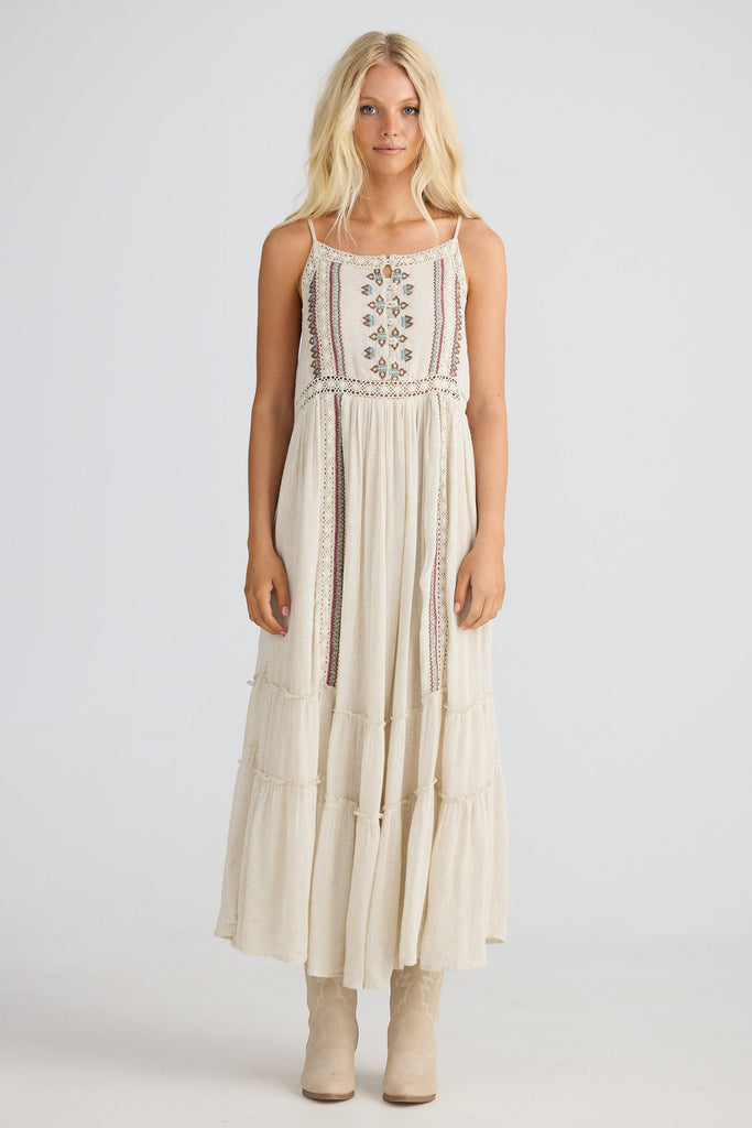 Woman wearing a long, light-colored dress with floral embroidery on a white background