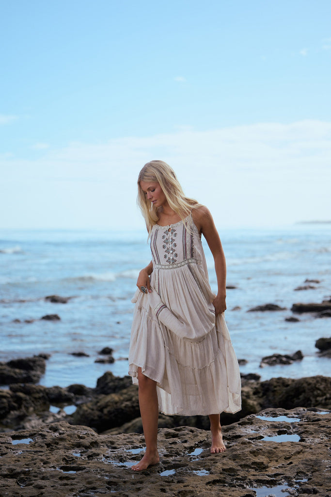 Woman in a flowing dress standing on a rocky beach with ocean and sky in the background