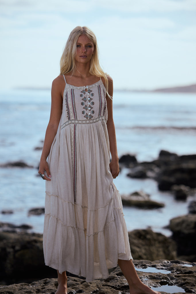 Woman in a light coloured dress standing on a rocky beach with ocean in the background