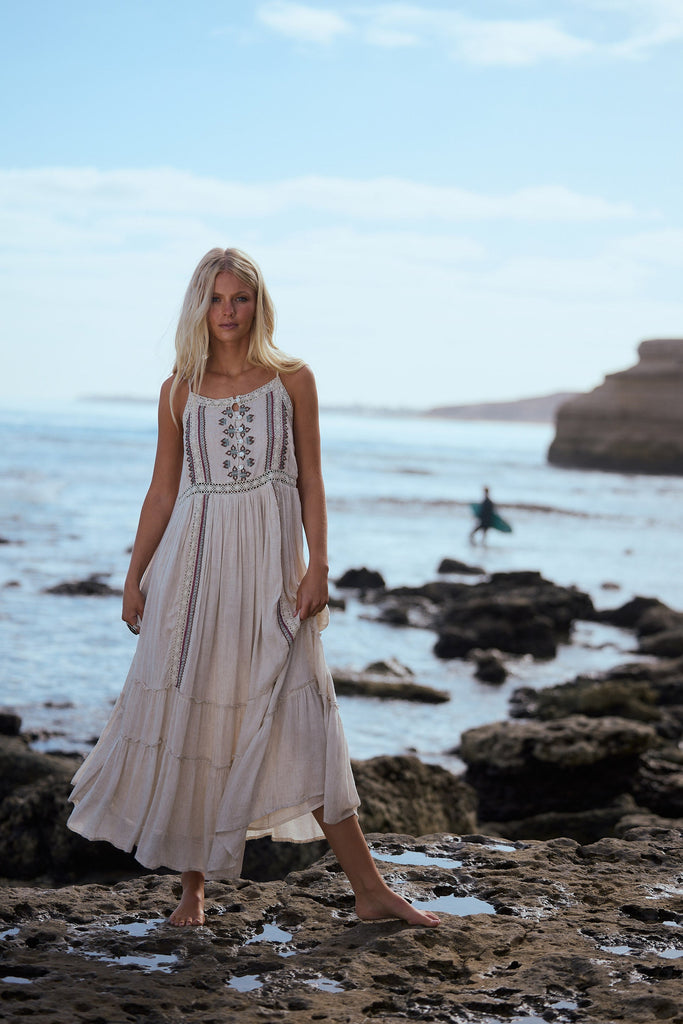 Woman in a light coloured dress standing on a rocky beach with ocean and sky in the background