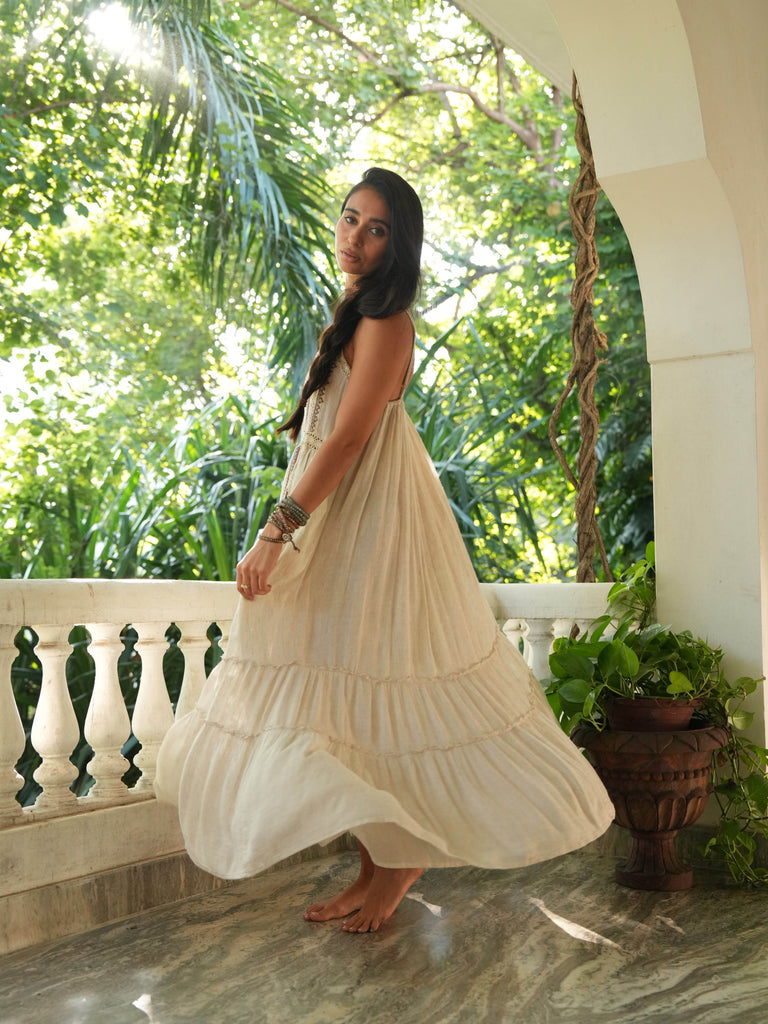 Woman in a flowing dress standing on a balcony with greenery in the background