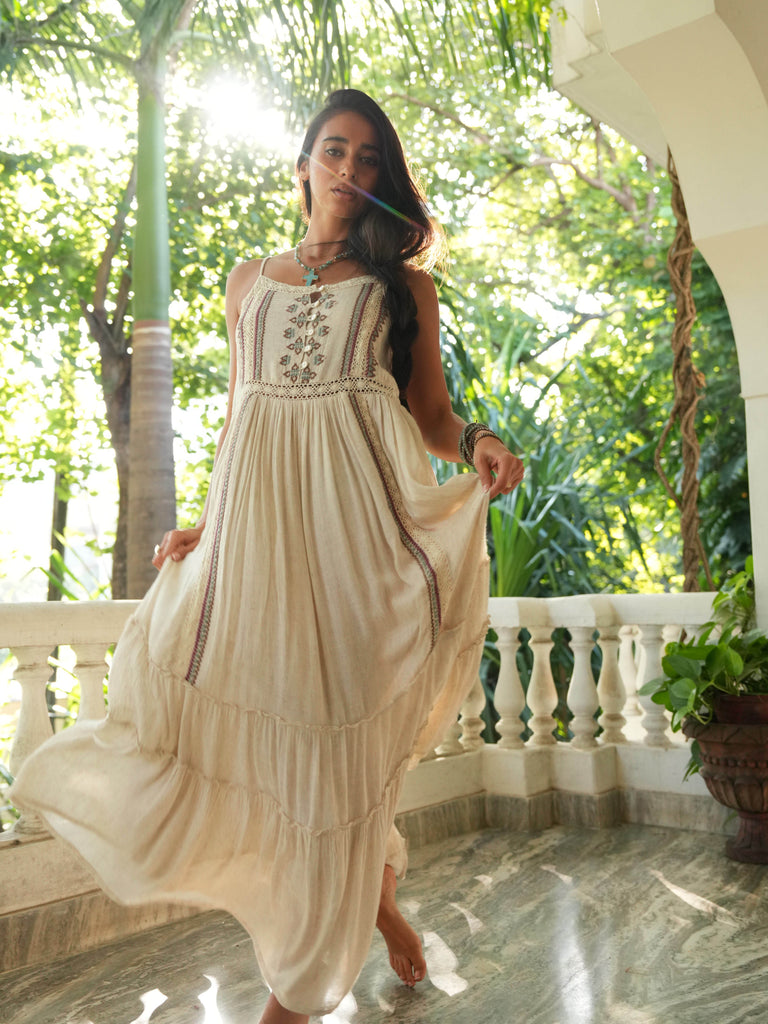 Woman in a long beige dress standing on a balcony with greenery in the background