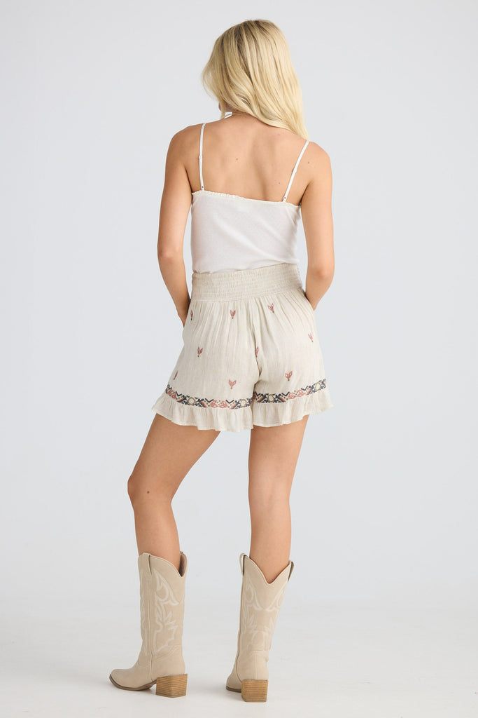 Woman wearing a white top and beige shorts with cowboy boots on a plain background