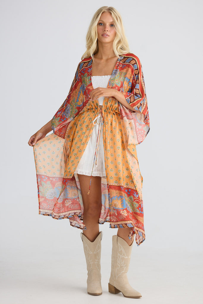 Woman wearing a colorful patterned cape with a white top and shorts and beige boots on a white background