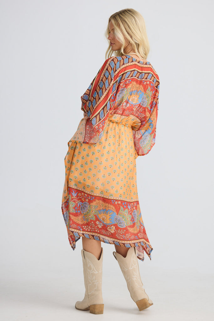 Woman wearing a colorful patterned cape with beige boots on a white background
