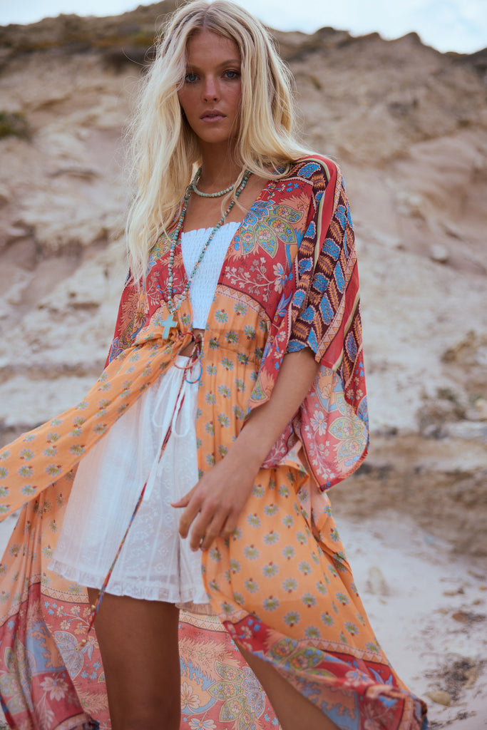 Woman wearing a colorful kimono over a white top and shorts in a desert setting