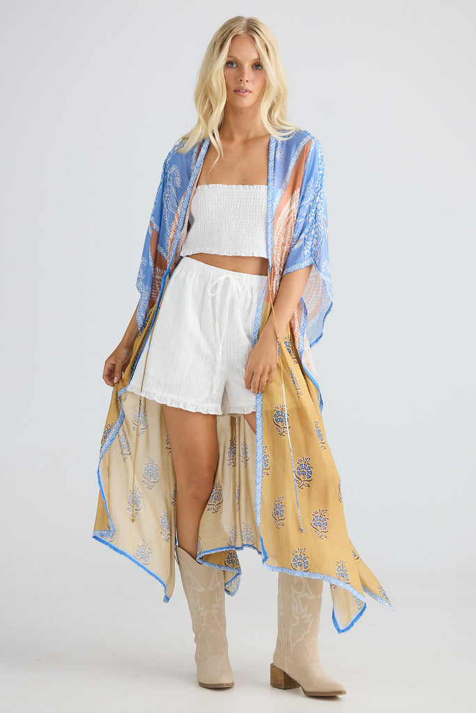 Woman wearing a long, patterned kimono over a white outfit on a plain background