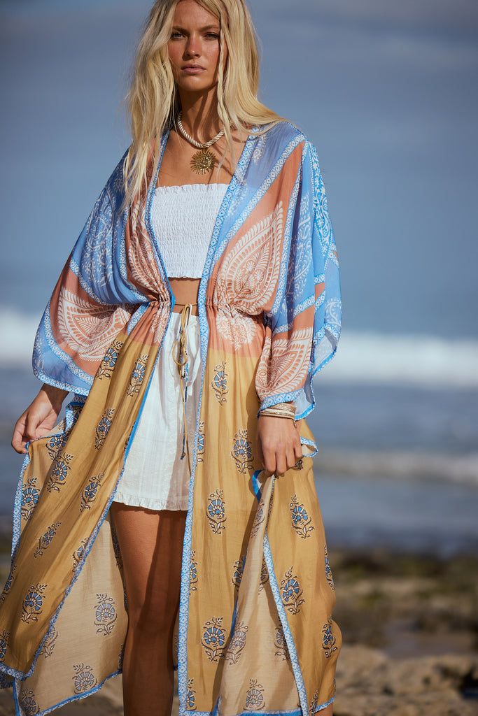 Woman wearing a patterned kimono standing on a beach with ocean in the background