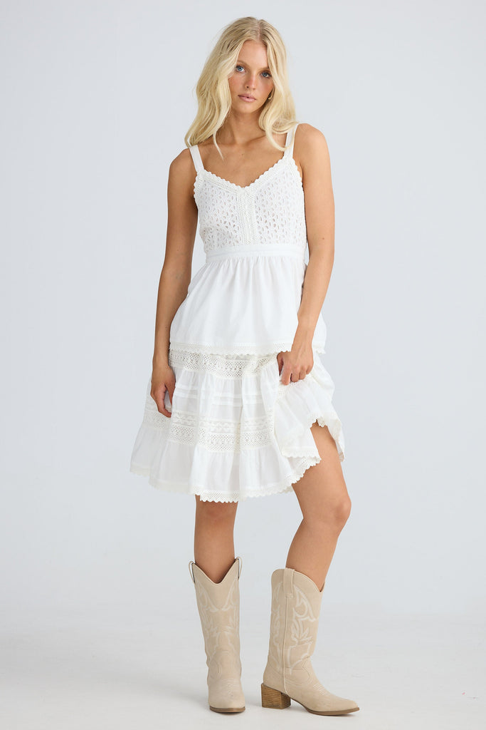 Woman wearing a white singlet and skirt with beige boots on a light gray background