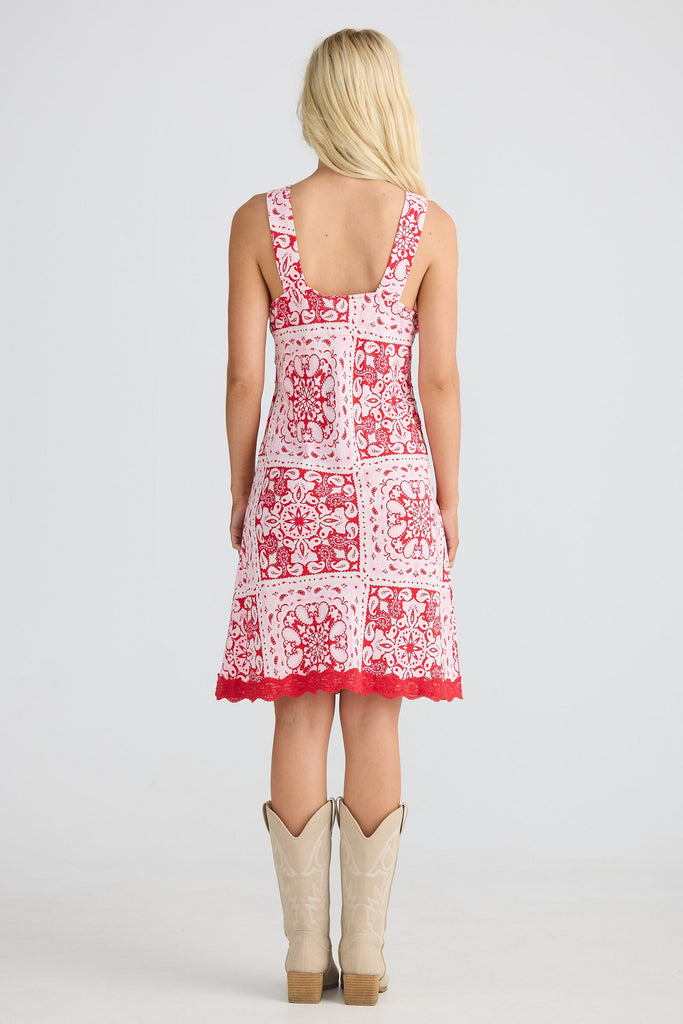 Woman wearing a red and white patterned dress with beige cowboy boots on a white background