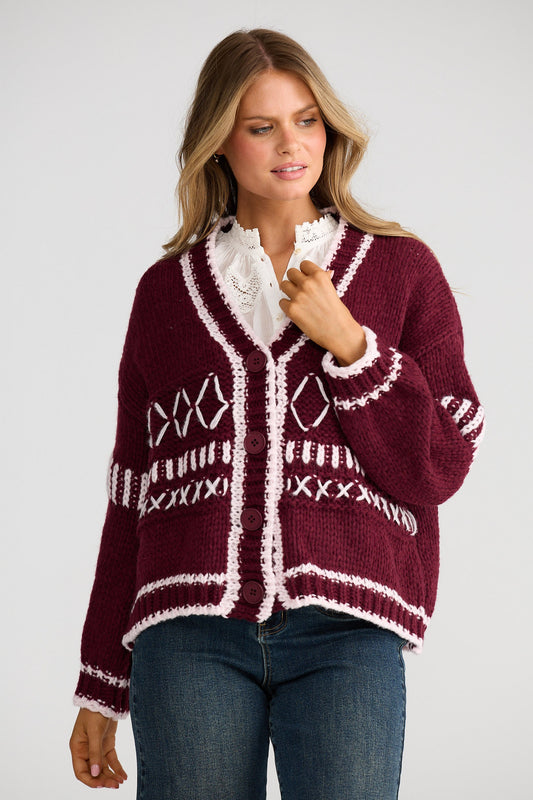 Woman wearing a burgundy cardigan with white patterns on a plain background