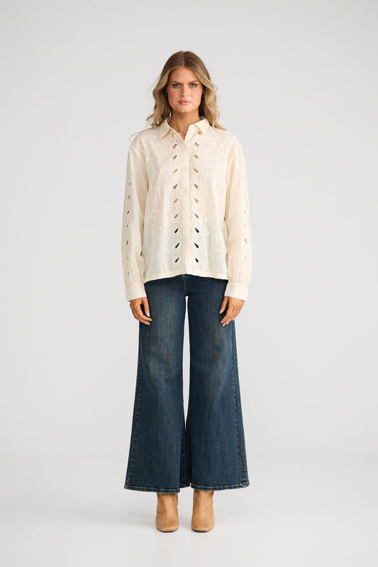 Woman wearing a beige blouse with lace details and wide-leg jeans on a white background