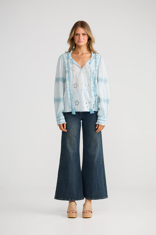 Woman wearing a light blue embroidered blouse and dark blue jeans on a white background