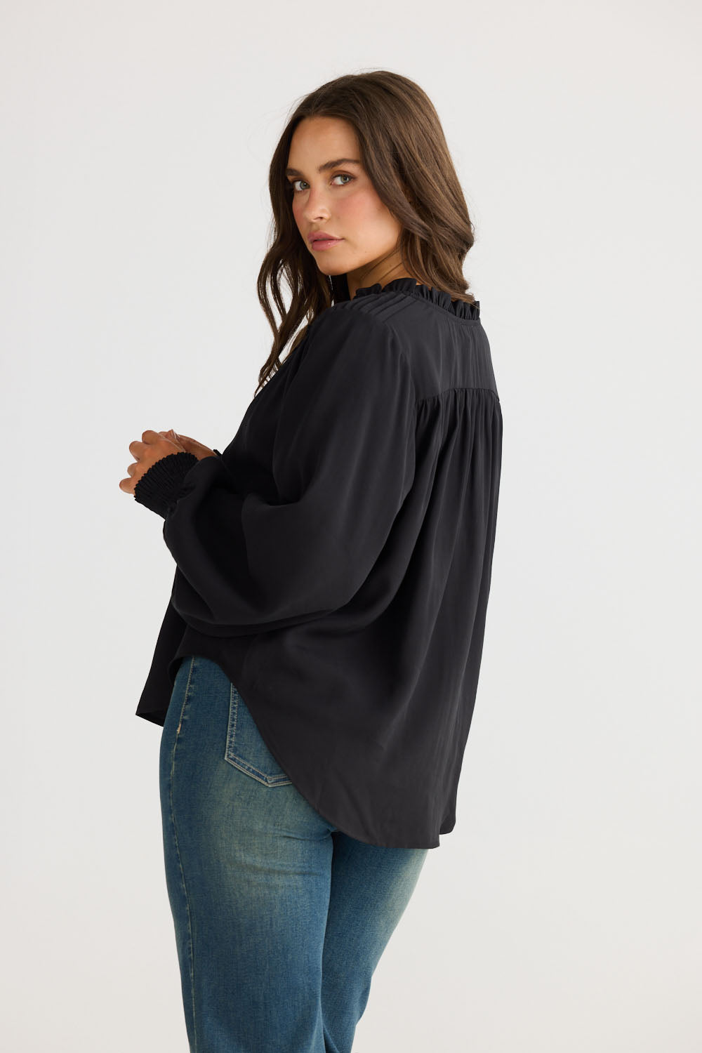 Model wearing Twilla Top in black with round neckline and mini ruffle trim, back view on white background