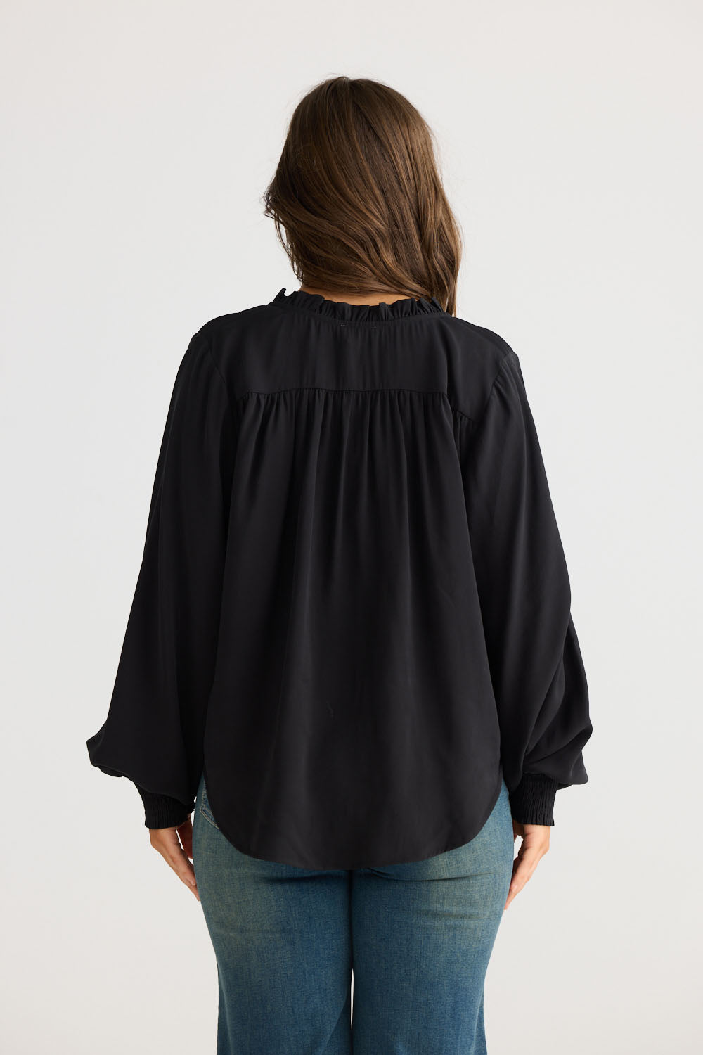 Model wearing Twilla Top in black with round neckline and mini ruffle trim, side view on white background