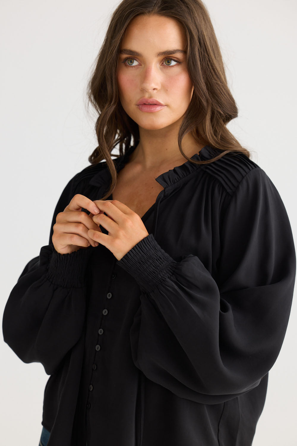 Model wearing Twilla Top in black with round neckline and mini ruffle trim, side view on white background