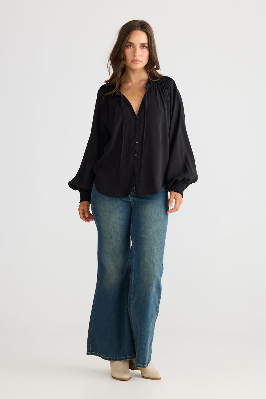 Model wearing Twilla Top in black with round neckline and mini ruffle trim, front view on white background