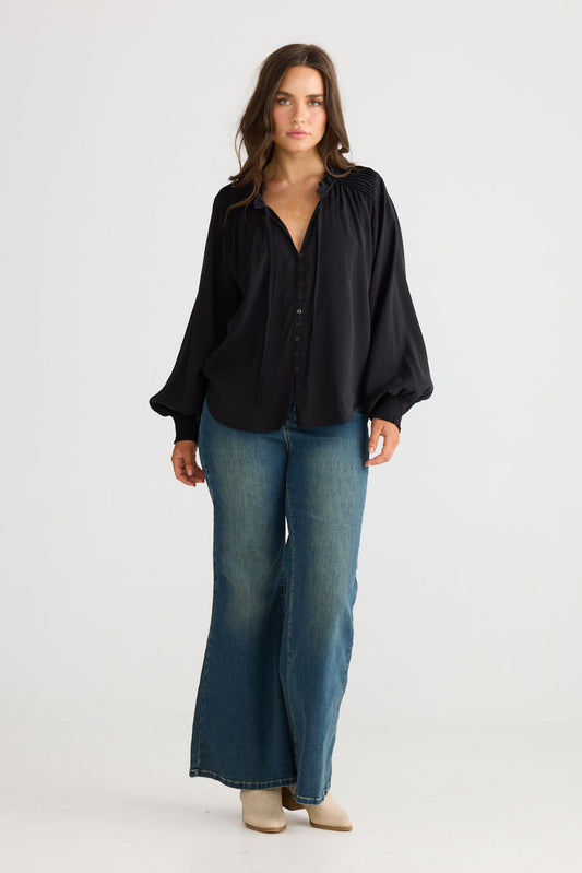 Model wearing Twilla Top in black with round neckline and mini ruffle trim, front view on white background
