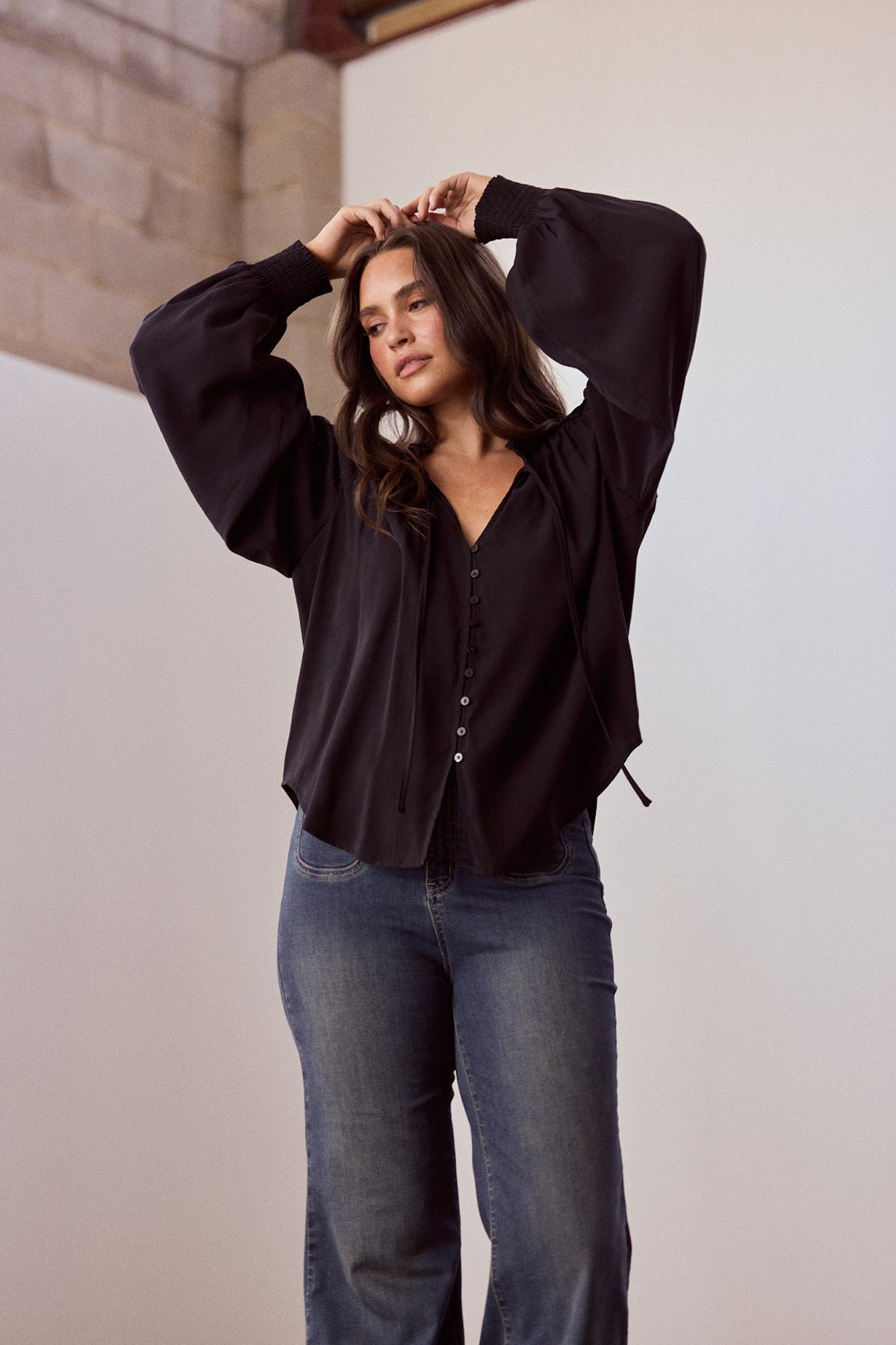 Model wearing Twilla Top in black with round neckline and mini ruffle trim, alternate view on white background