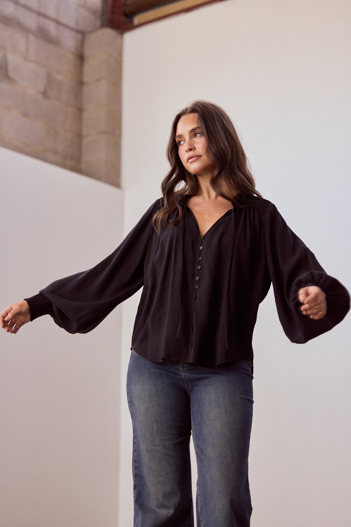 Model wearing Twilla Top in black with round neckline and mini ruffle trim, alternate view on white background
