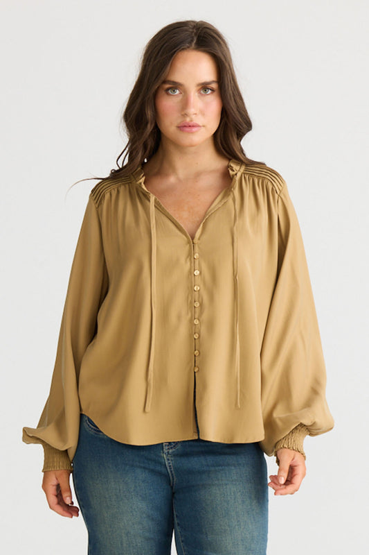 Model wearing Twilla Top in camel with round neckline and mini ruffle trim, side view on white background