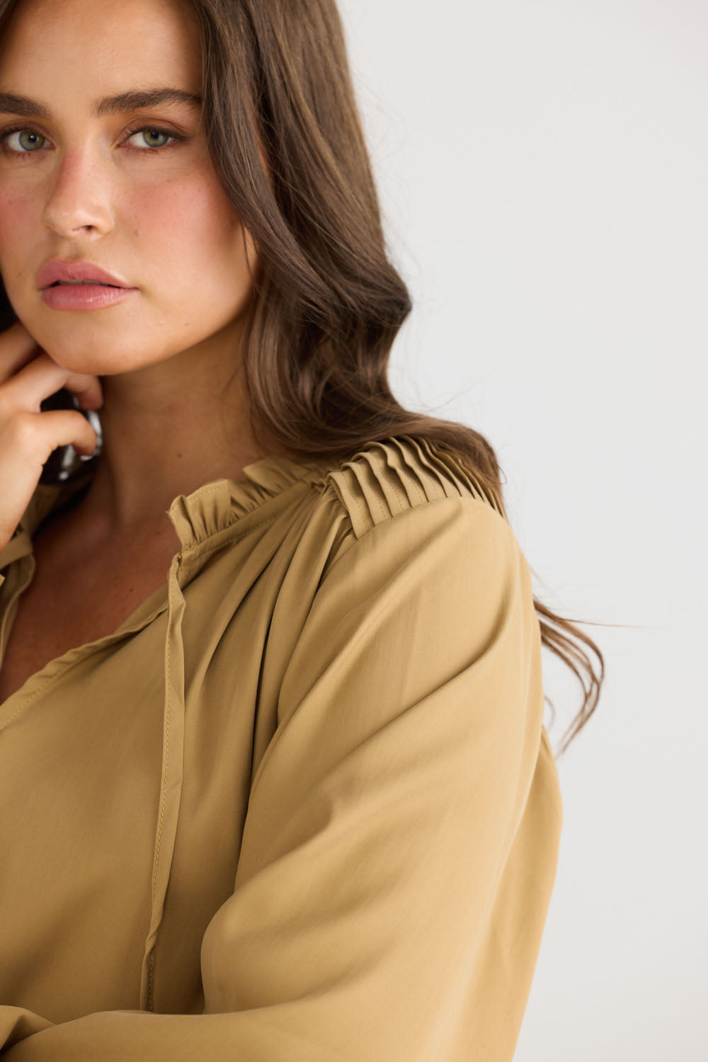 Close-up of Twilla Top in camel showing round neckline and mini ruffle trim, detail view on white background