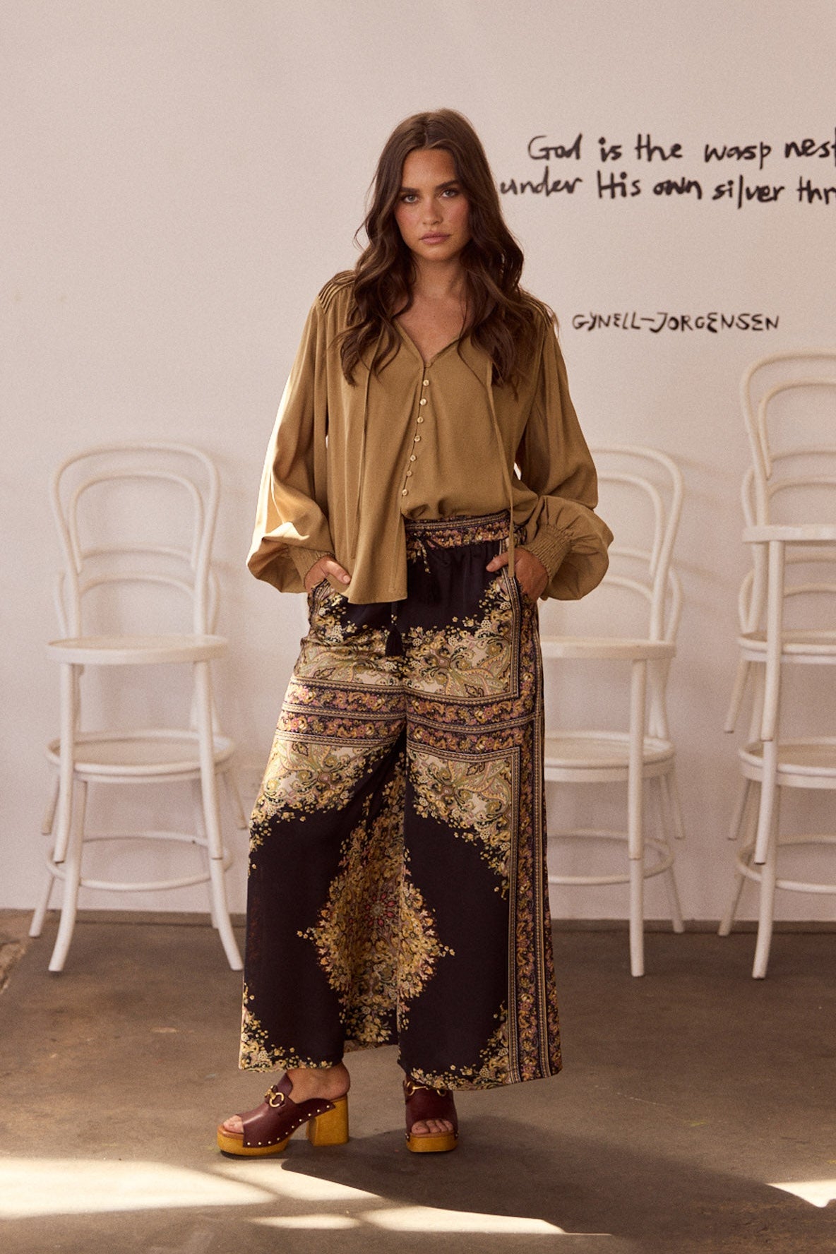 Model wearing Twilla Top in camel with round neckline and mini ruffle trim, back view on white background