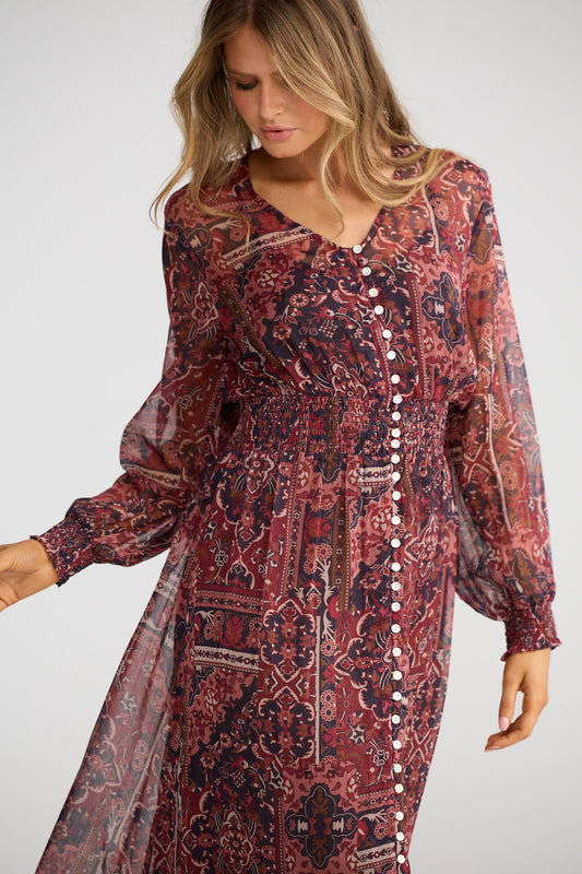 Woman wearing a patterned dress with long sleeves on a plain background