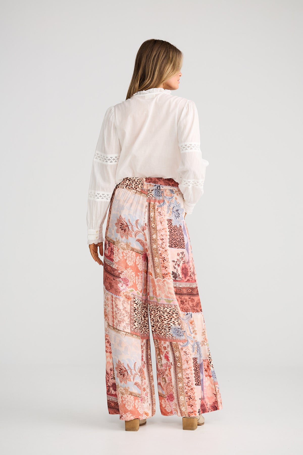 Woman wearing a white blouse and patterned pants on a plain background