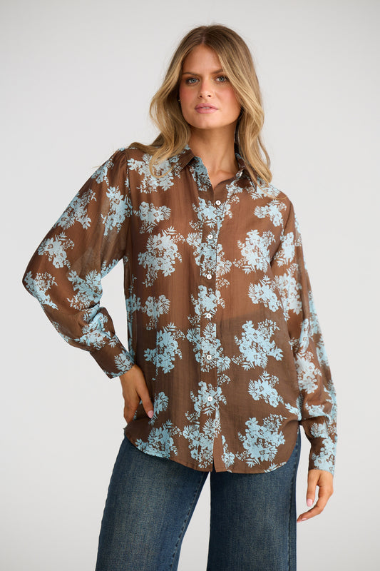 Woman wearing a brown floral blouse with blue flowers on a white background