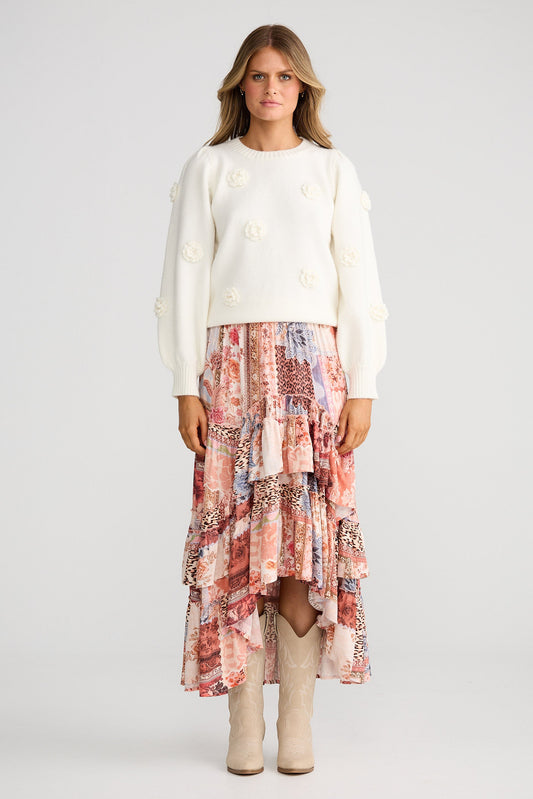 Woman wearing a white sweater and patterned skirt on a plain background