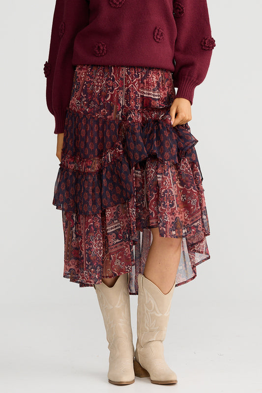 Person wearing a burgundy sweater, patterned skirt, and beige boots on a white background