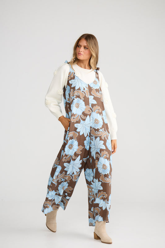 Woman wearing a floral jumpsuit with a white shirt underneath on a white background