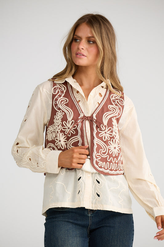 Woman wearing a cream blouse with intricate red embroidery on a plain background