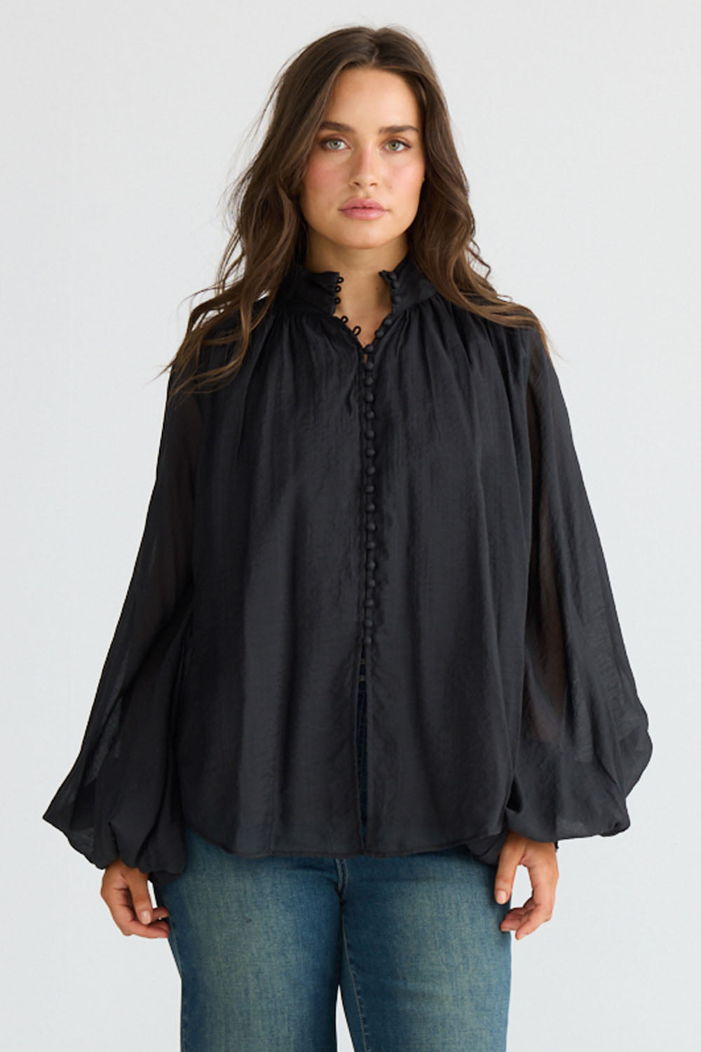Model wearing Sylva Blouse in black with high collar with ruched details, front view on white background