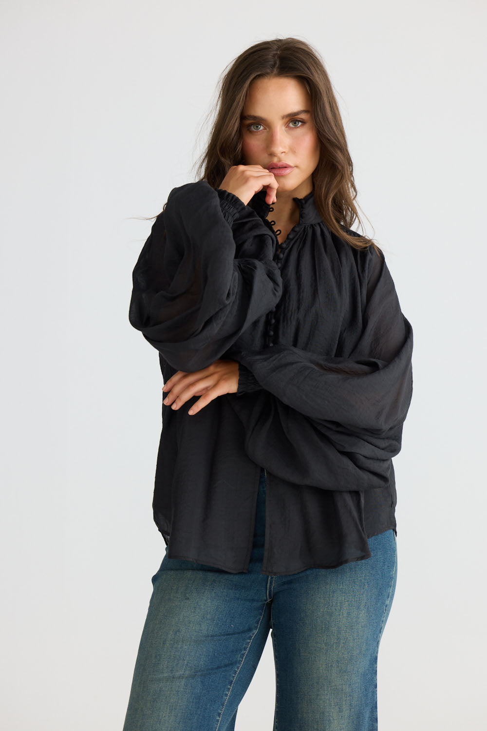 Model wearing Sylva Blouse in black with high collar with ruched details, side view on white background