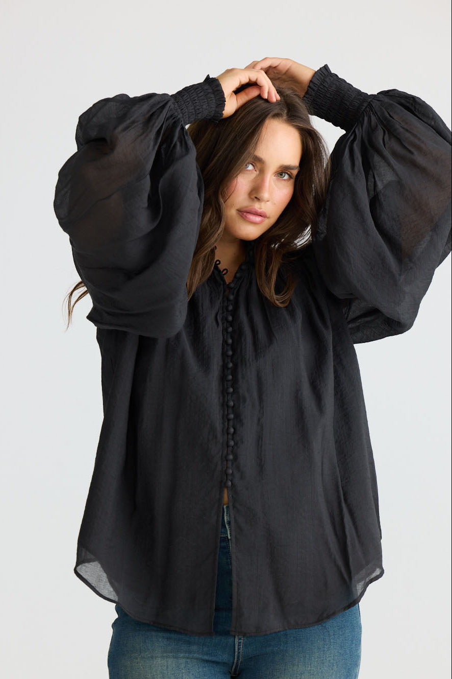 Model wearing Sylva Blouse in black with high collar with ruched details, front view on white background